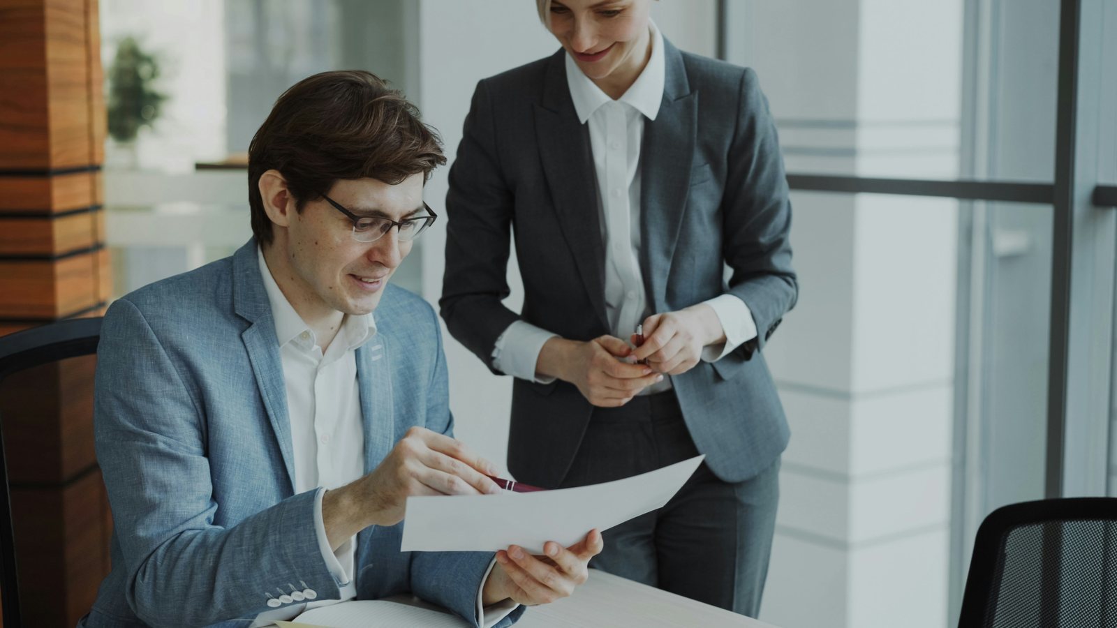 Two business colleagues in an office reviewing a printed document together to agree on payment terms