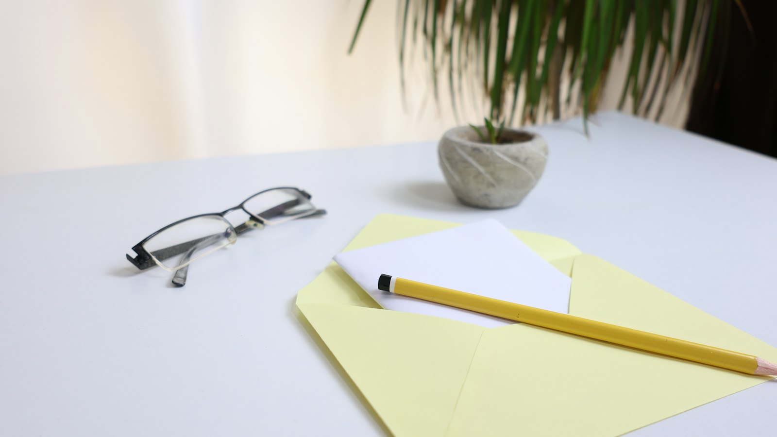 A pair of glasses and a pencil resting on a yellow envelope on a clean office desk, ready for a commercial collection letter