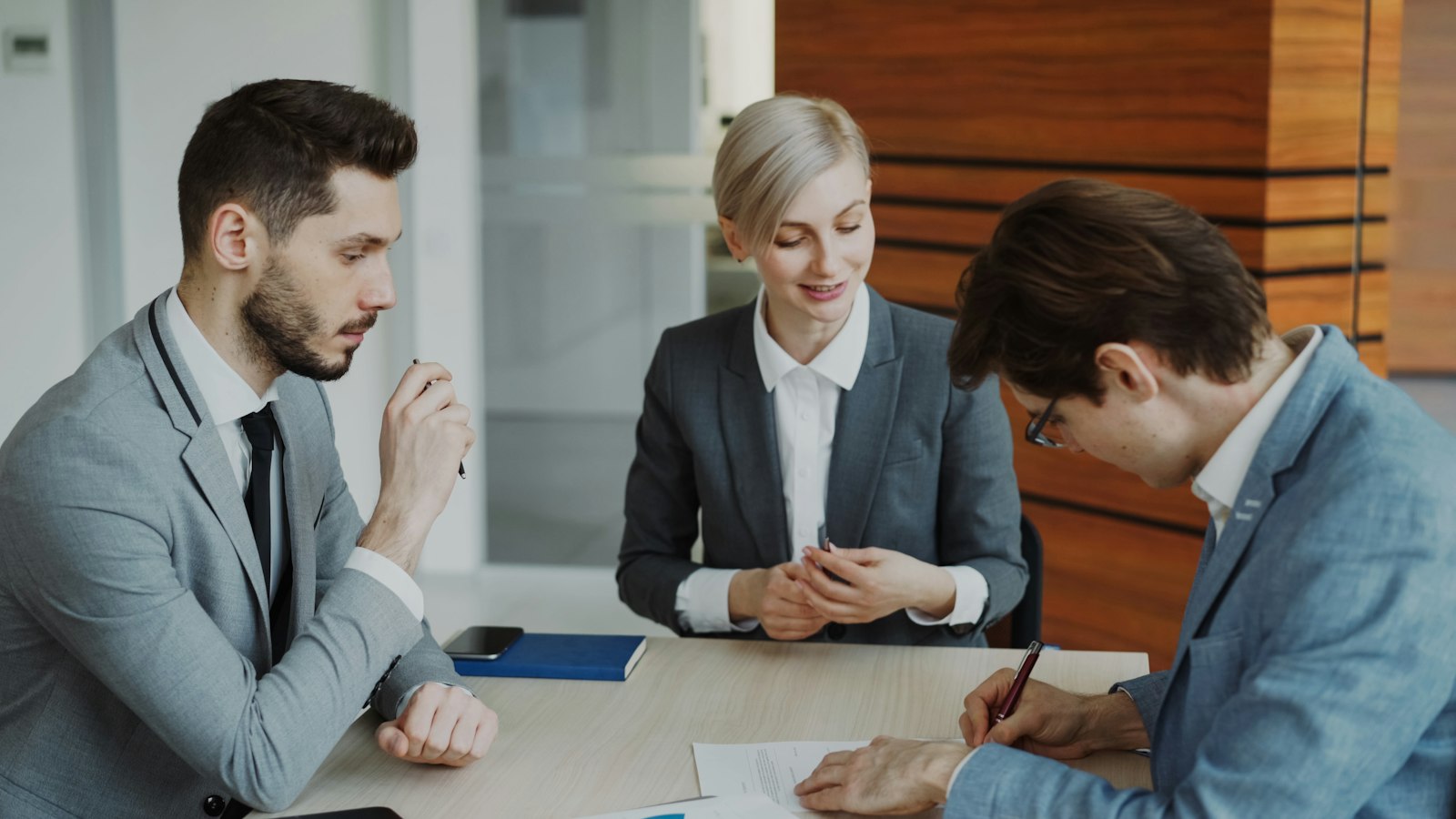 Three business people at a table as one signs a document, as when a creditor files a proof of claim in a customer bankruptcy