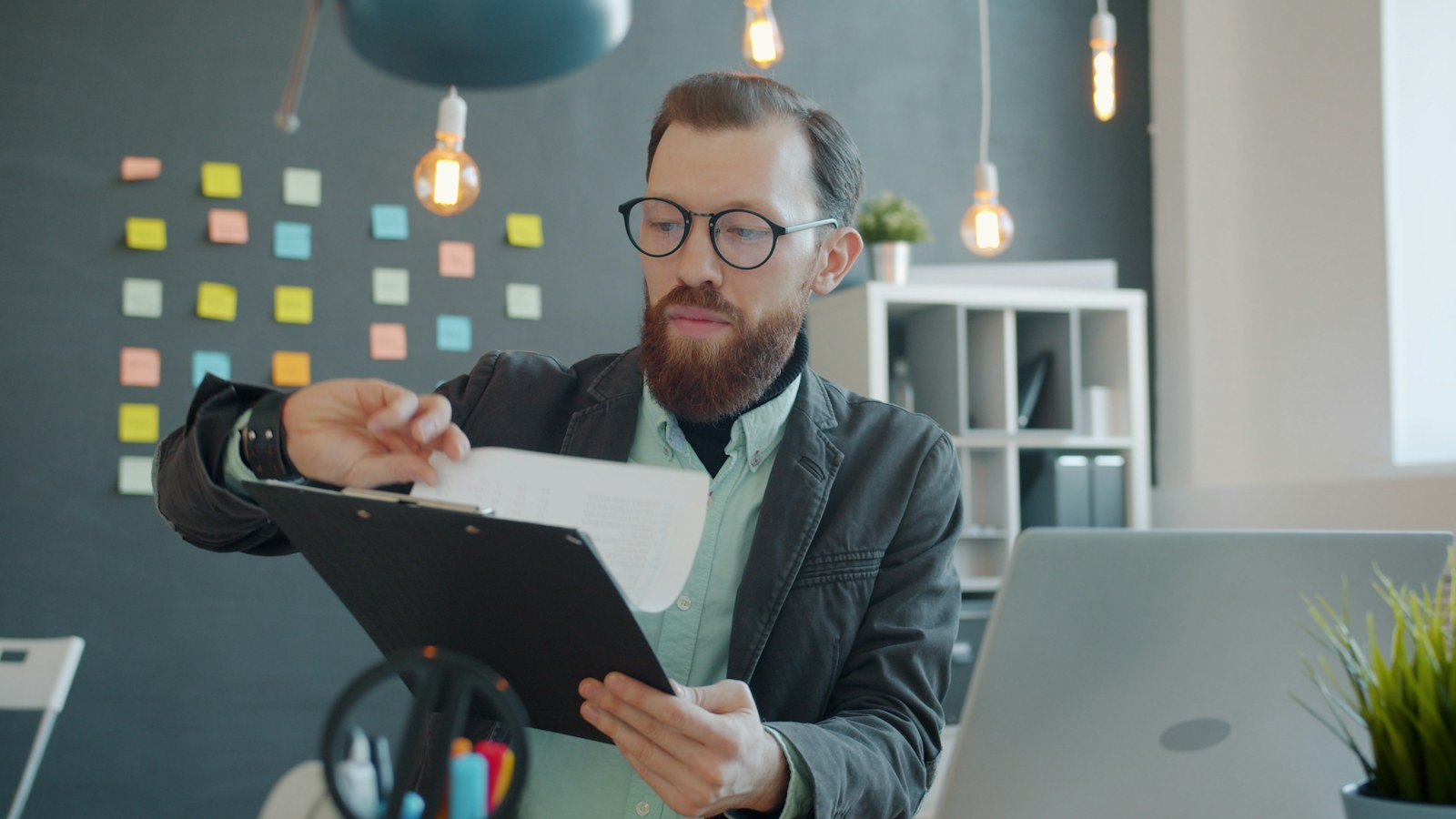 A credit manager in glasses reviewing a printed final demand letter on a clipboard at an office desk