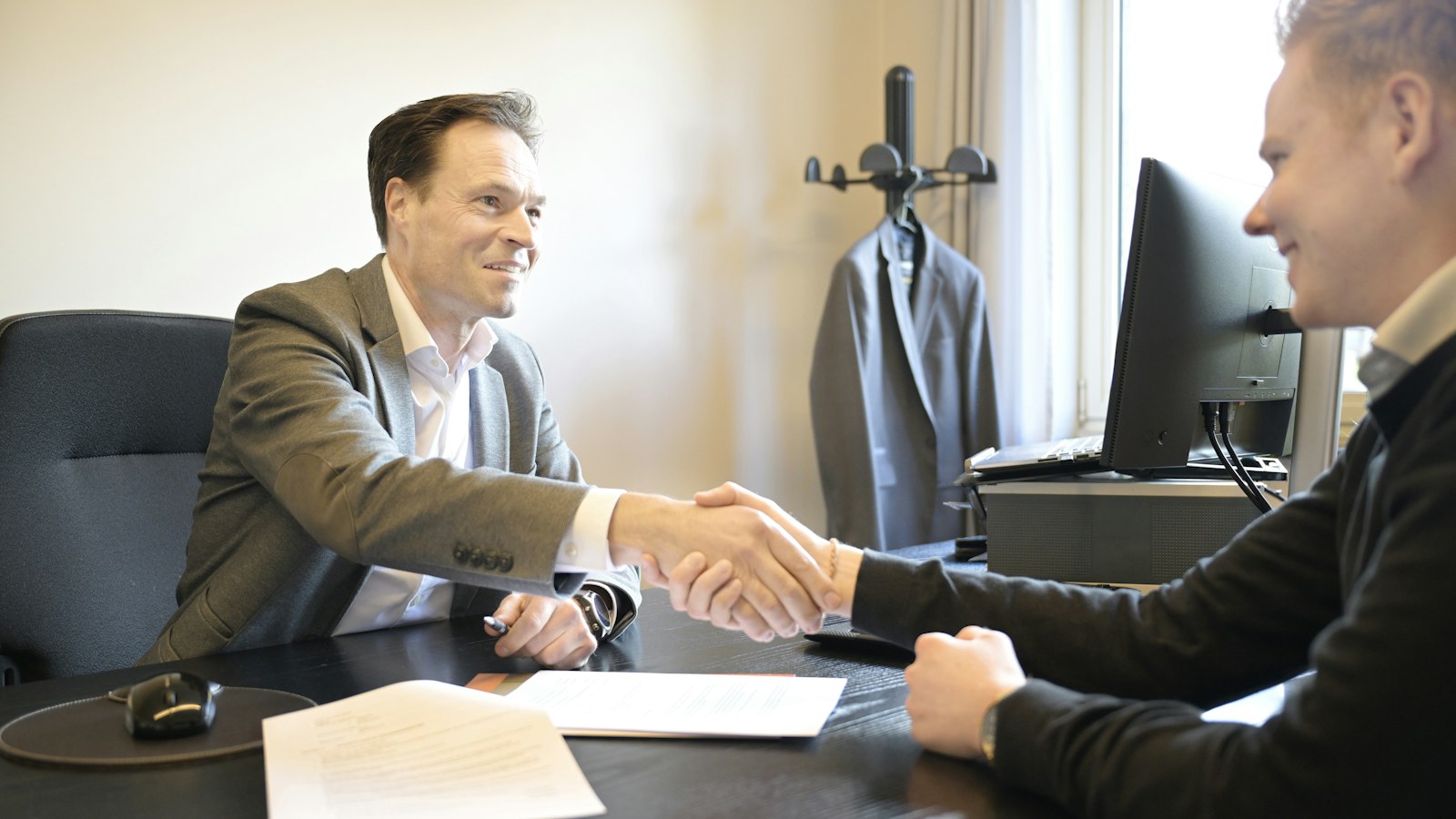 Two business people shaking hands across an office desk over a credit application before extending business credit
