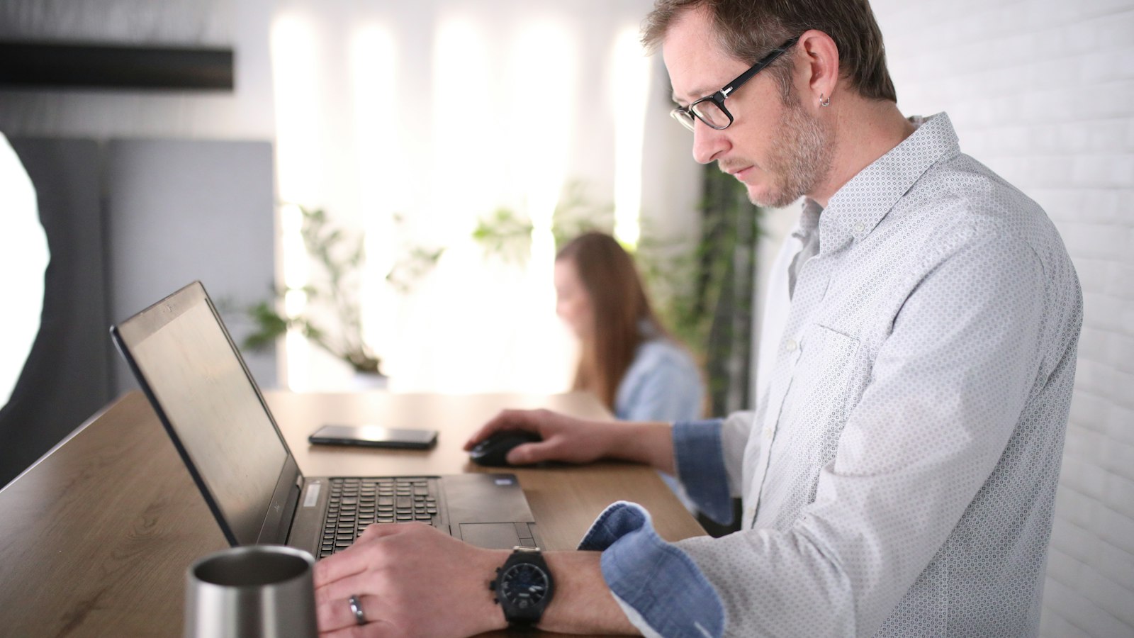 A man in glasses searching records on a laptop at an office desk, tracing a customer who has gone quiet